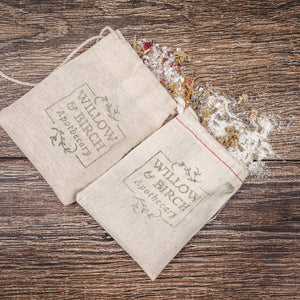 Natural bath salts in rustic linen bags labeled Willow & Birch Apothecary, spilled on a wooden surface. This image captures the essence of natural Dead Sea salts and the best bath crystals and therapeutic salts for a relaxing spa salt bath.