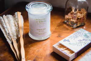 Scented soy candle by Willow & Birch Apothecary with apothecary jar of rose petals, Victorian style fan, and book of decorative matches