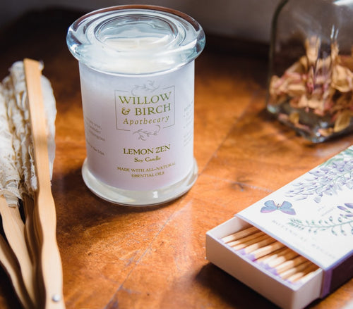 Scented soy candle by Willow & Birch Apothecary with apothecary jar of rose petals, Victorian style fan, and book of decorative matches