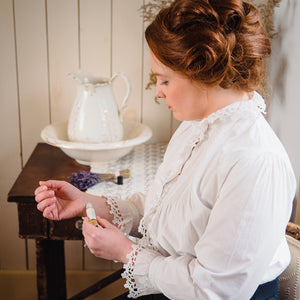 Woman in a vintage white blouse applying all natural perfume oils, capturing the essence of non toxic perfume application and enjoying plant based perfumes for a signature scent.