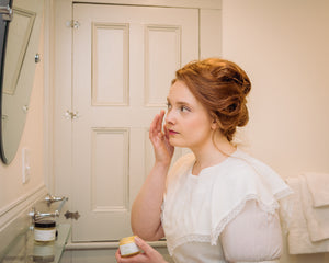Woman in Victorian dress applying moisturizer face cream