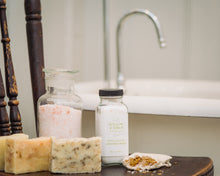 Natural bath salts, scented bath soap bars, and botanical mineral bath soak in front of antique clawfoot bathtub