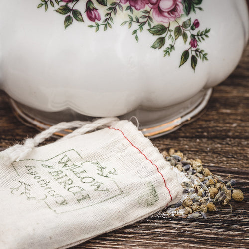Natural Dead Sea salts and dried herbs spill from a rustic cloth bag beside a vintage floral ceramic teapot, epitomizing the best bath salts for relaxing. Perfect for a soothing epsom salt bath experience.